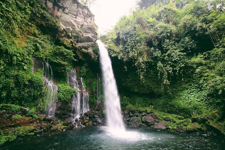Waterfall cascading into a pool surrounded by rocky cliffs and green tropical vegetation